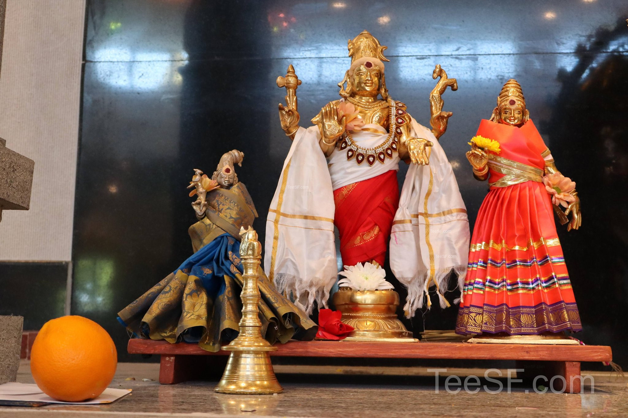 A shrine scene with brass lamps and colorful deity figures.